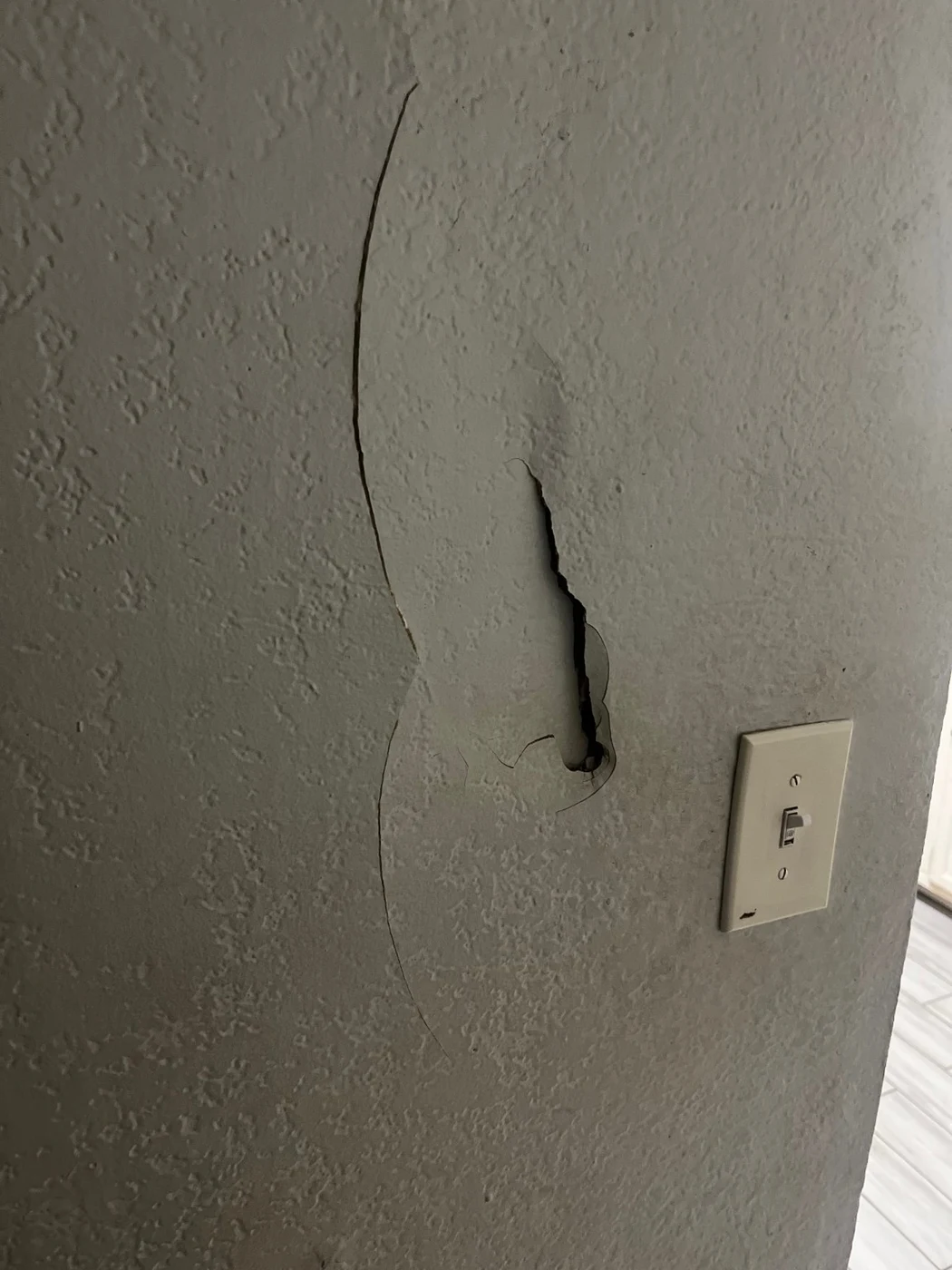 Cracked and broken drywall near a light switch before repair in Arlington